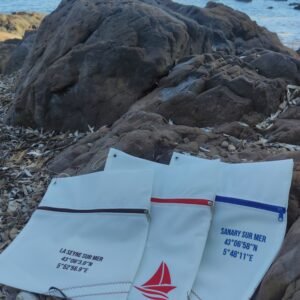 Pochettes en voile de bateau recyclée, personnalisées en rouge, bleu et marron, photographiées en bord de mer à La Seyne-sur-Mer.